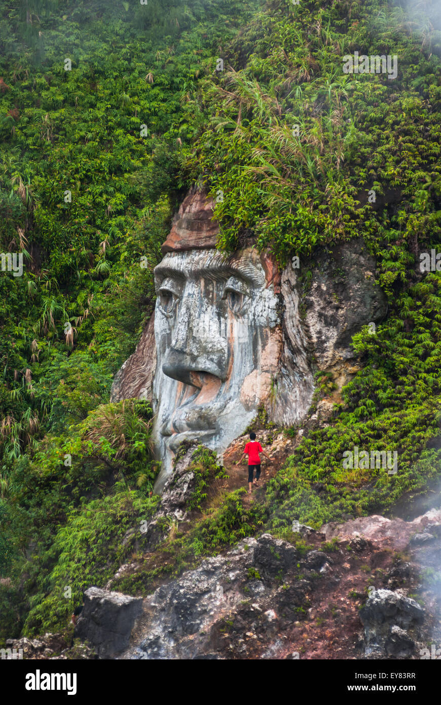 Ein Besucher wird in der Nähe einer riesigen Gesichtsformation gesehen, die den Charakter von Toar (eine uralte Figur) im Bukit Kasih in North Sulawesi, Indonesien, veranschaulicht. Stockfoto