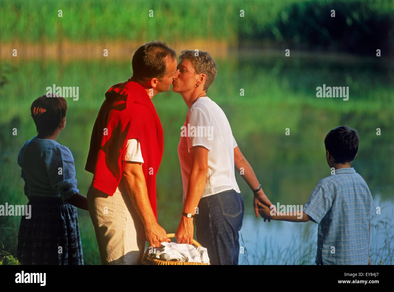 Vierköpfige Familie Picknick in der Nähe von Landschaft Teich in Bayern, Deutschland-Mutter und Vater küssen Stockfoto