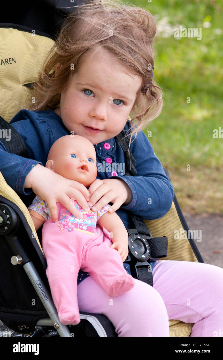Glückliche kleine Mädchen im Kinderwagen kuscheln ihre Puppe Stockfoto
