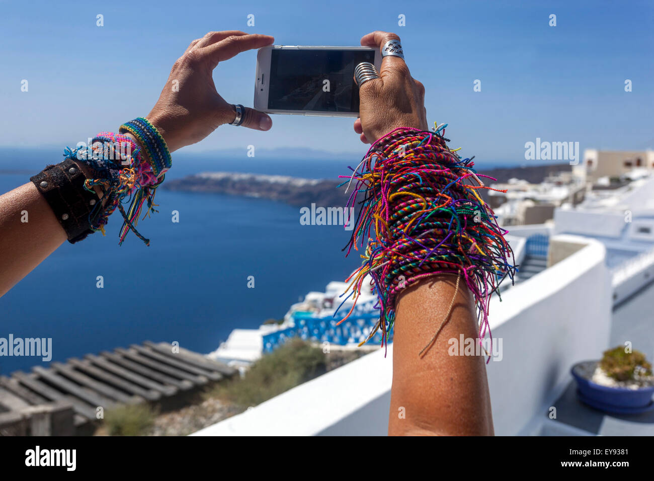 Eine große Anzahl von gestrickten Frauen Armbänder auf dem Mädchen Hände EINER Frau, die ein Foto Telefon Santorini Landschaft Griechenland Bunte Freundschaftsarmbänder Stockfoto