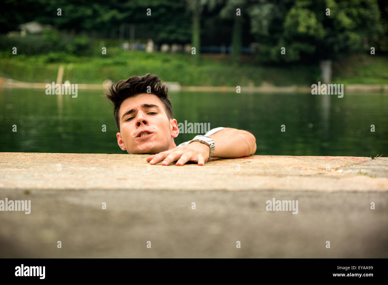 Hübscher junger Mann in einem See verzweifelt, sich selbst zu retten, indem man etwas auf dem Boden gefallen Stockfoto