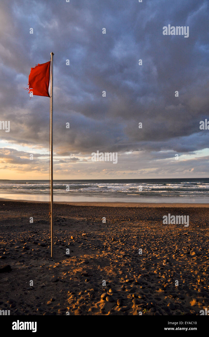 Ausgefranste Warnfahne am roten Strand flammend im Wind, mit Wellen und  Wolken bei Sonnenuntergang bei Ebbe am Strand von Famara (Lanzarote,  Kanarische Inseln, Spanien Stockfotografie - Alamy