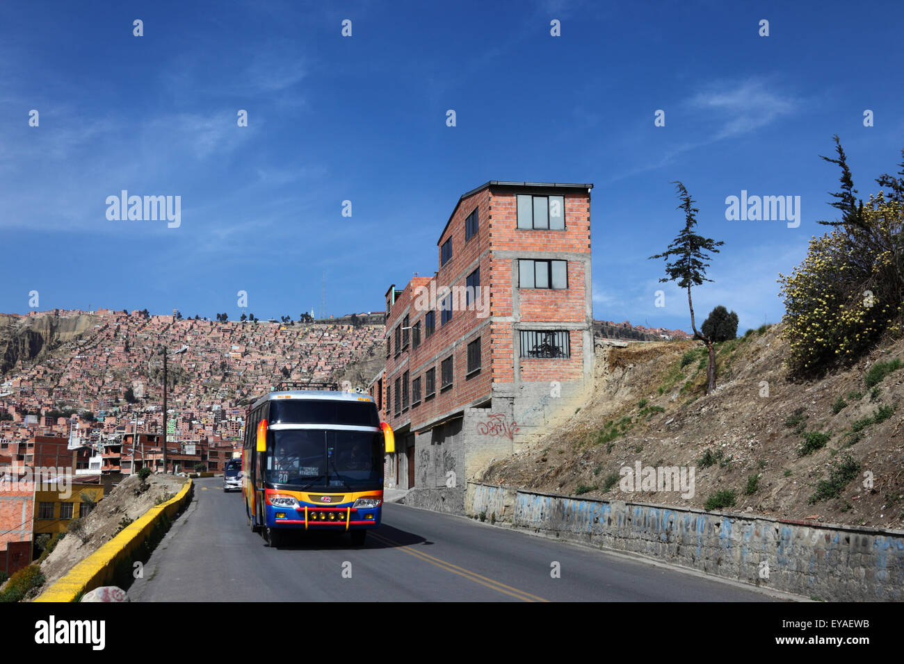 Bus mit öffentlichen Verkehrsmitteln, der bergauf an einem Backsteingebäude im Stadtvorort La Paz, Bolivien, vorbeifährt Stockfoto