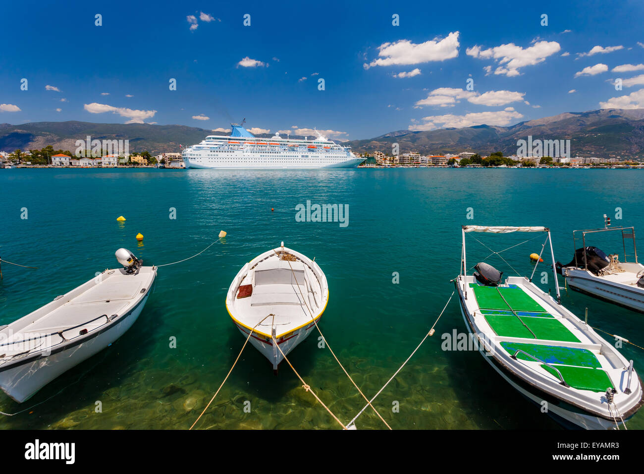 Große Kreuzfahrtschiff vor Anker im Hafen mit kleinen Fischen Boote im Vordergrund vor einem blauen Himmel und Wolken in Griechenland Stockfoto