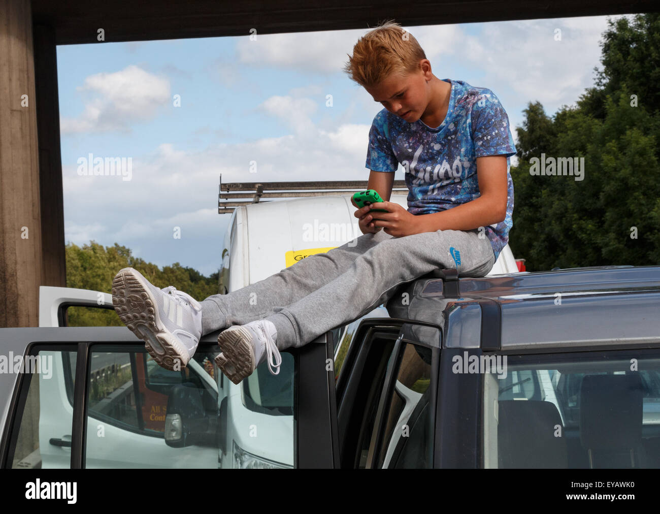 Ein kleiner Junge gelangweilter Teenager sitzen auf dem Dach eines Fahrzeugs in einer Linie des ruhenden Verkehrs im Autobahn Stau Stockfoto