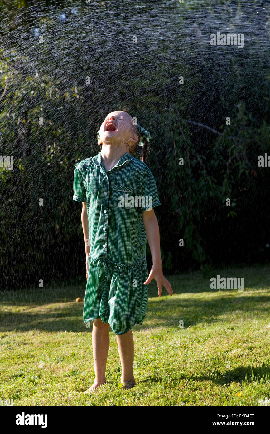 Mädchen im grünen Kleid spielen unter einem Wasser Sprinkler. Stockfoto