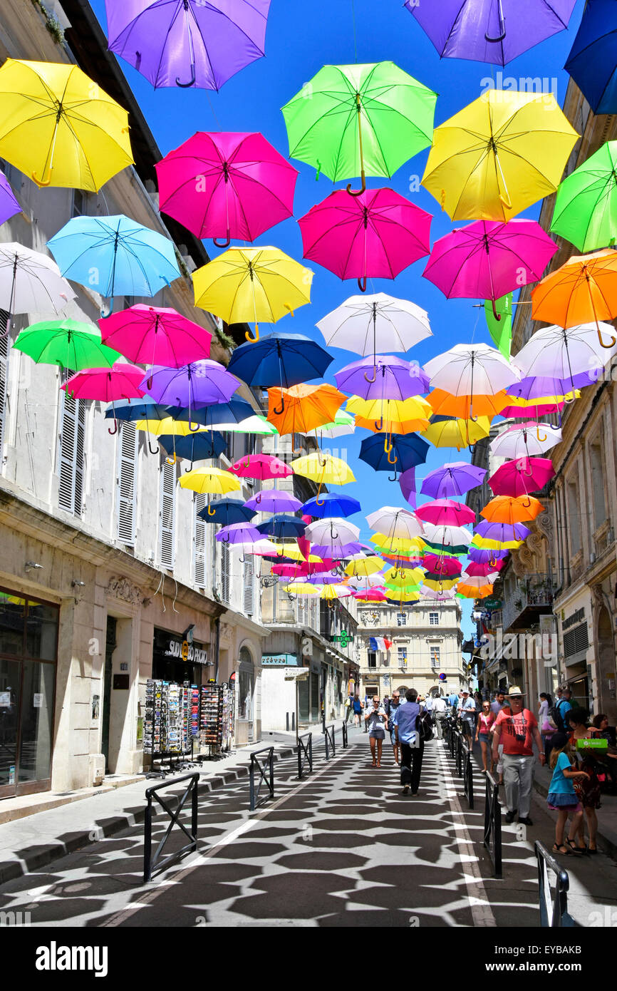 Blauer Himmel und Regenschirmfarben in der Street Art-Ausstellung in der antiken Stadt Arles Frankreich Provence werfen sich wiederholende Schattenmuster auf französische Einkaufsstraße Stockfoto