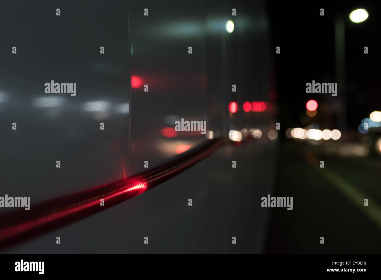 Eine Nahaufnahme von einem roten Lichtschlauch geht entlang einer Wand außerhalb ein Baugebiet in der Nacht mit Autos Rückleuchten verschwommen im Stockfoto