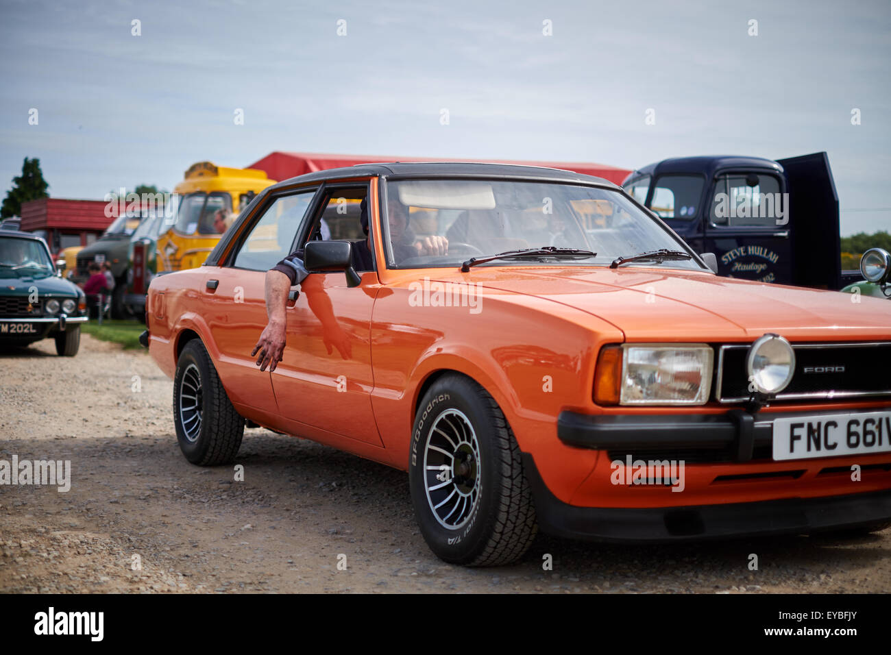 Ein Mann mit fettigen Händen fährt in einem Jahrgang vorbei Orange Ford Cortina bei der Ripon Car Rally Stockfoto