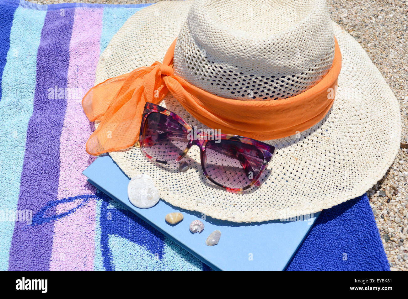 Strohhut-Sonnenbrille und ein Buch am Strand an einem sonnigen Tag Stockfoto