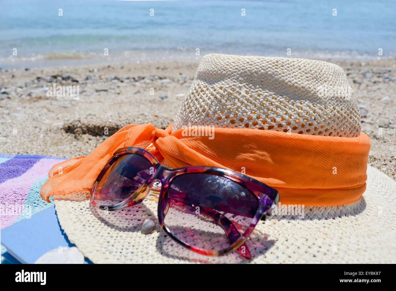 Strohhut-Sonnenbrille und ein Buch mit Meer im Hintergrund an einem sonnigen Tag am Strand Stockfoto