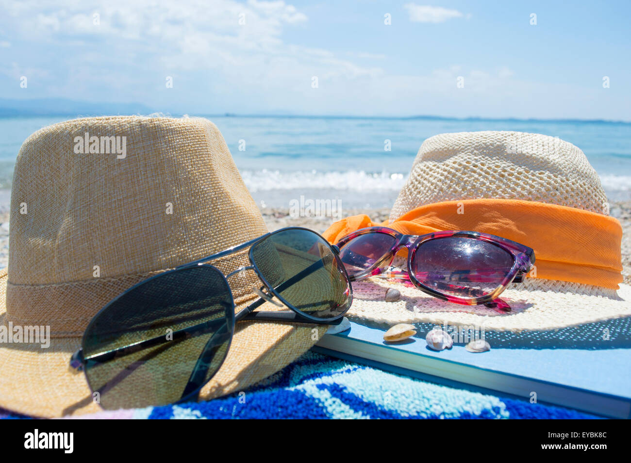 Zwei Strohhüte Sonnenbrille und ein Buch mit Meer im Hintergrund an einem sonnigen Tag am Strand Stockfoto