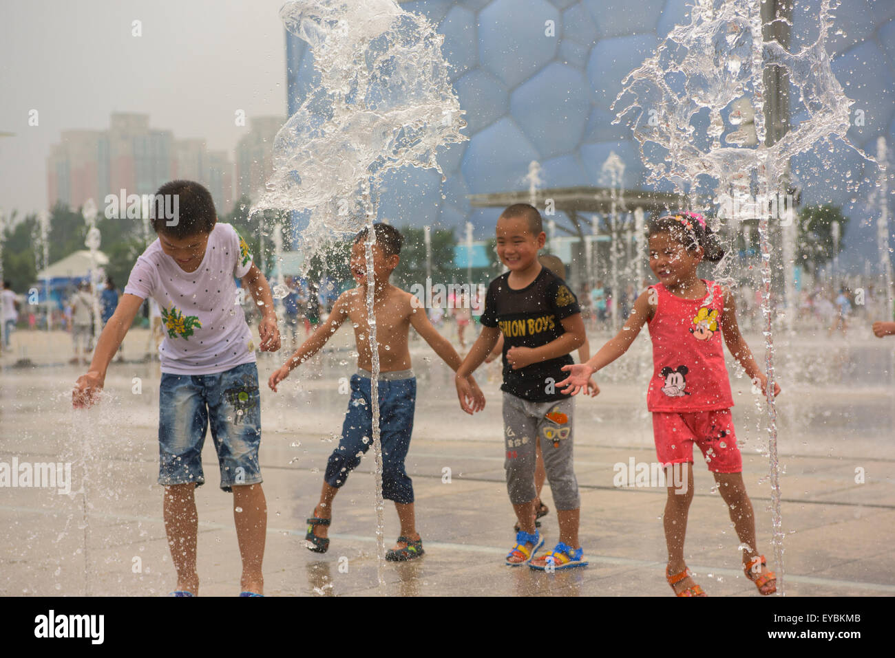 Kinder mit Spaß spielen unter der Wassersprenger vor der Water Cube im Beijing Olympic Park - Juli 2015 Stockfoto