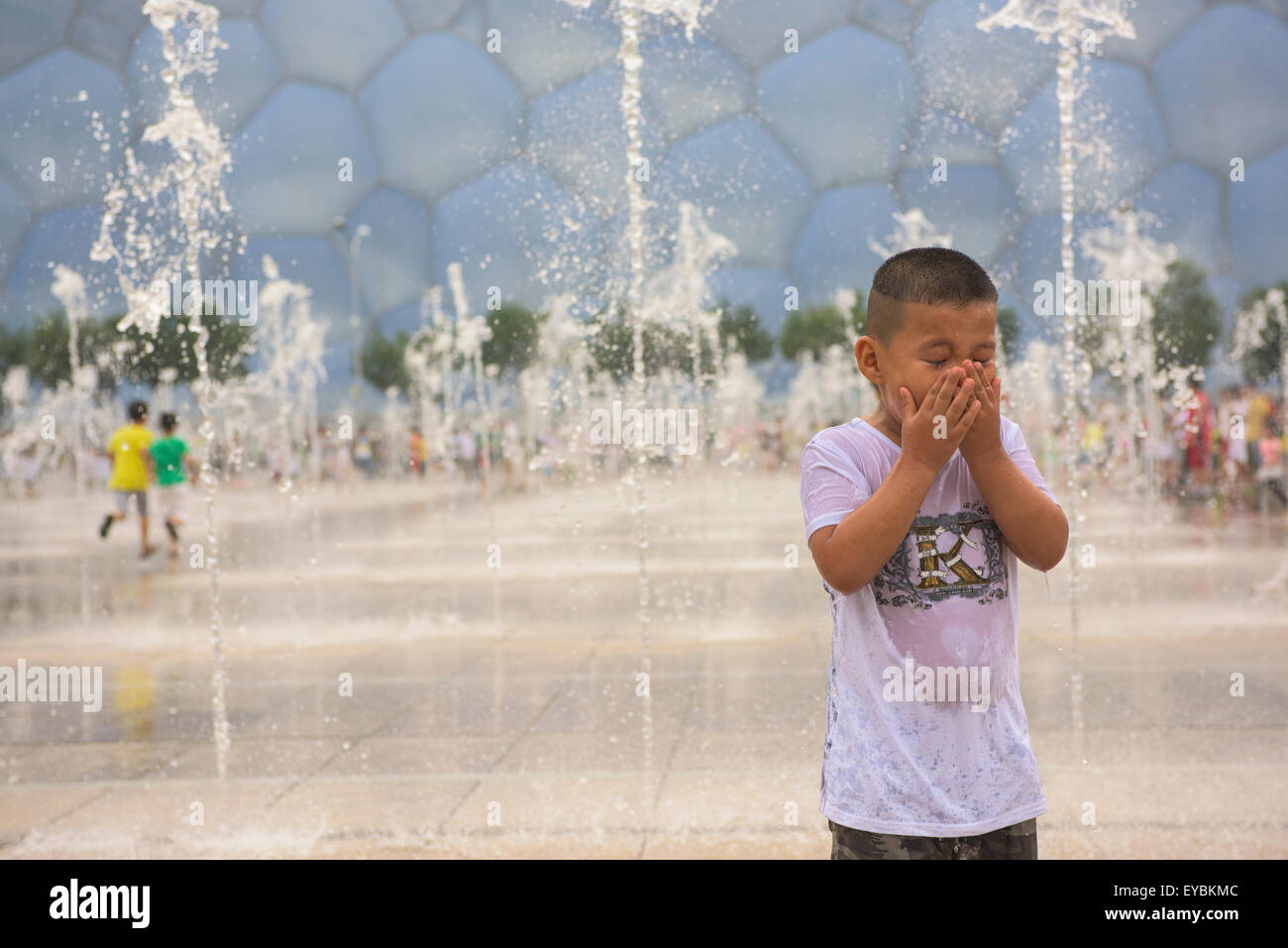 Junge mit Spaß spielen unter der Wassersprenger vor der Water Cube im Beijing Olympic Park - Juli 2015 Stockfoto
