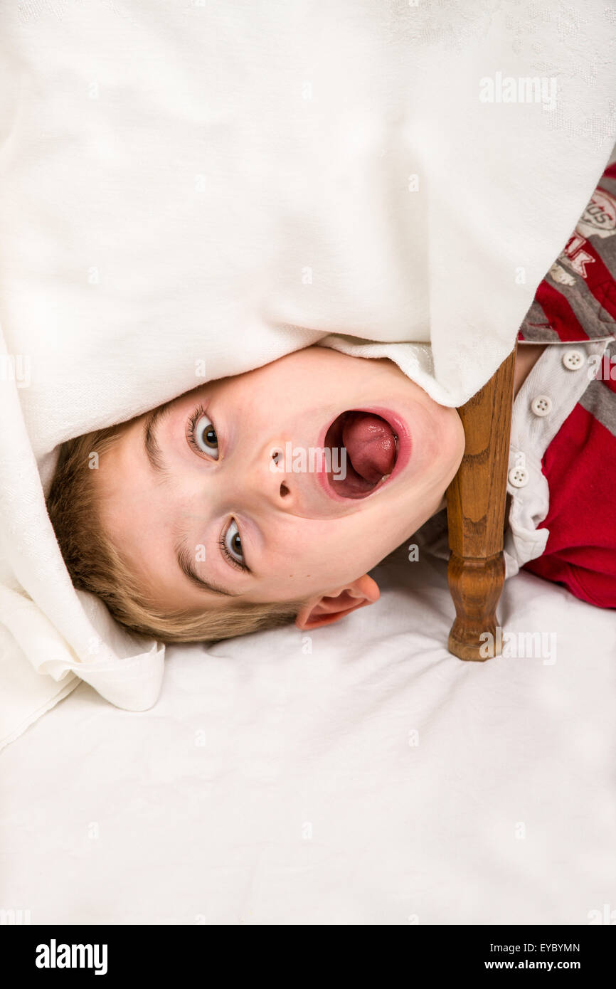 Sechs Jahre alten Jungen Spaß machen Gesichter unter einem überdachten Tisch Stockfoto