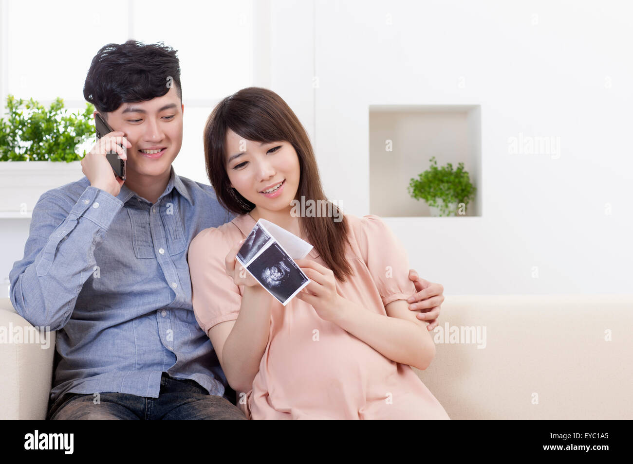 Junger Mann halten Handys und sitzen mit schwangeren Frau Stockfoto