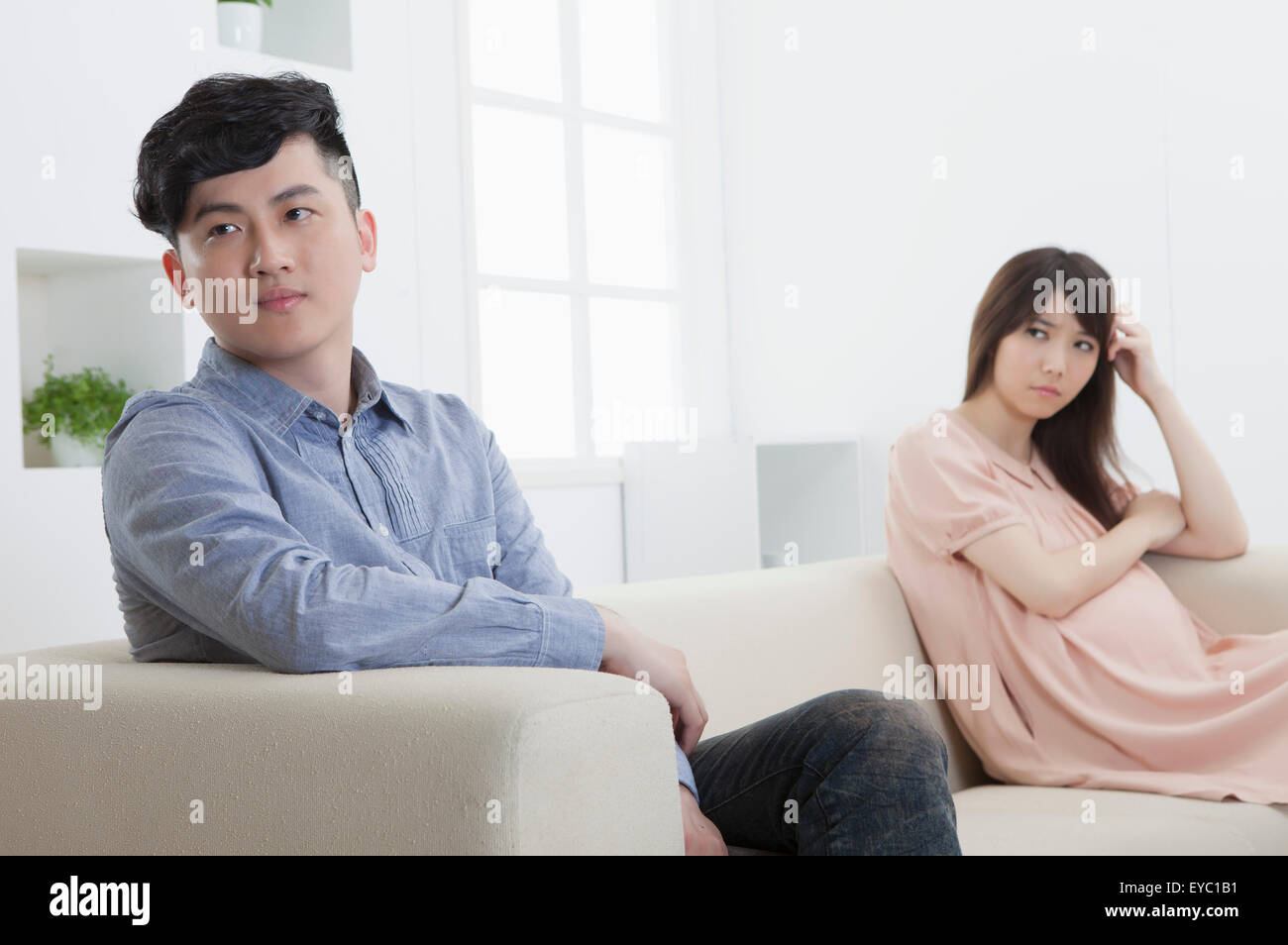 Junger Mann und schwangere Frau sitzt auf dem Sofa mit schlechter Laune, Stockfoto