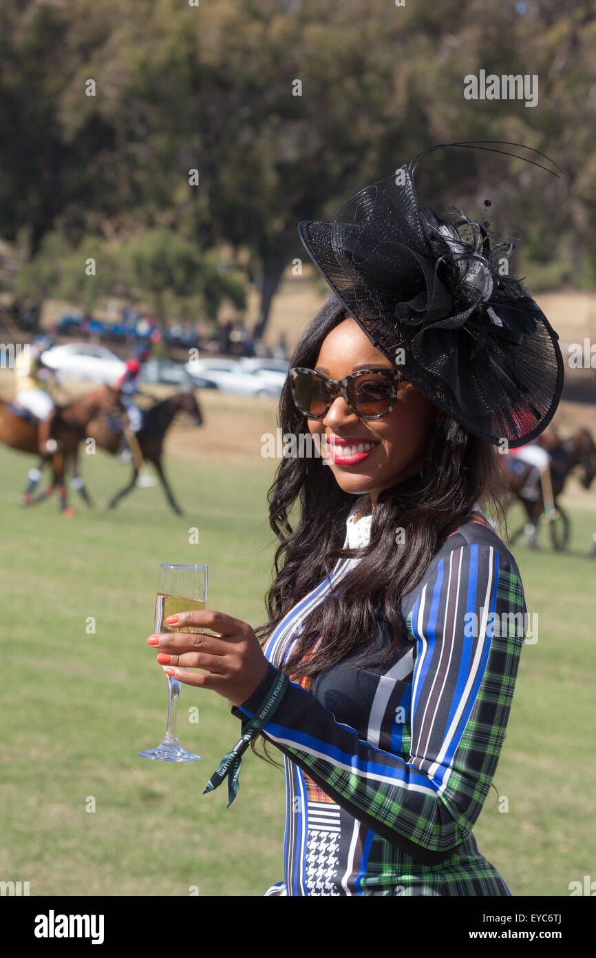 Eine Frau in einem schwarzen Hut und hellen Kleid mit einem Glas Champagner beim Polo ansehen Stockfoto