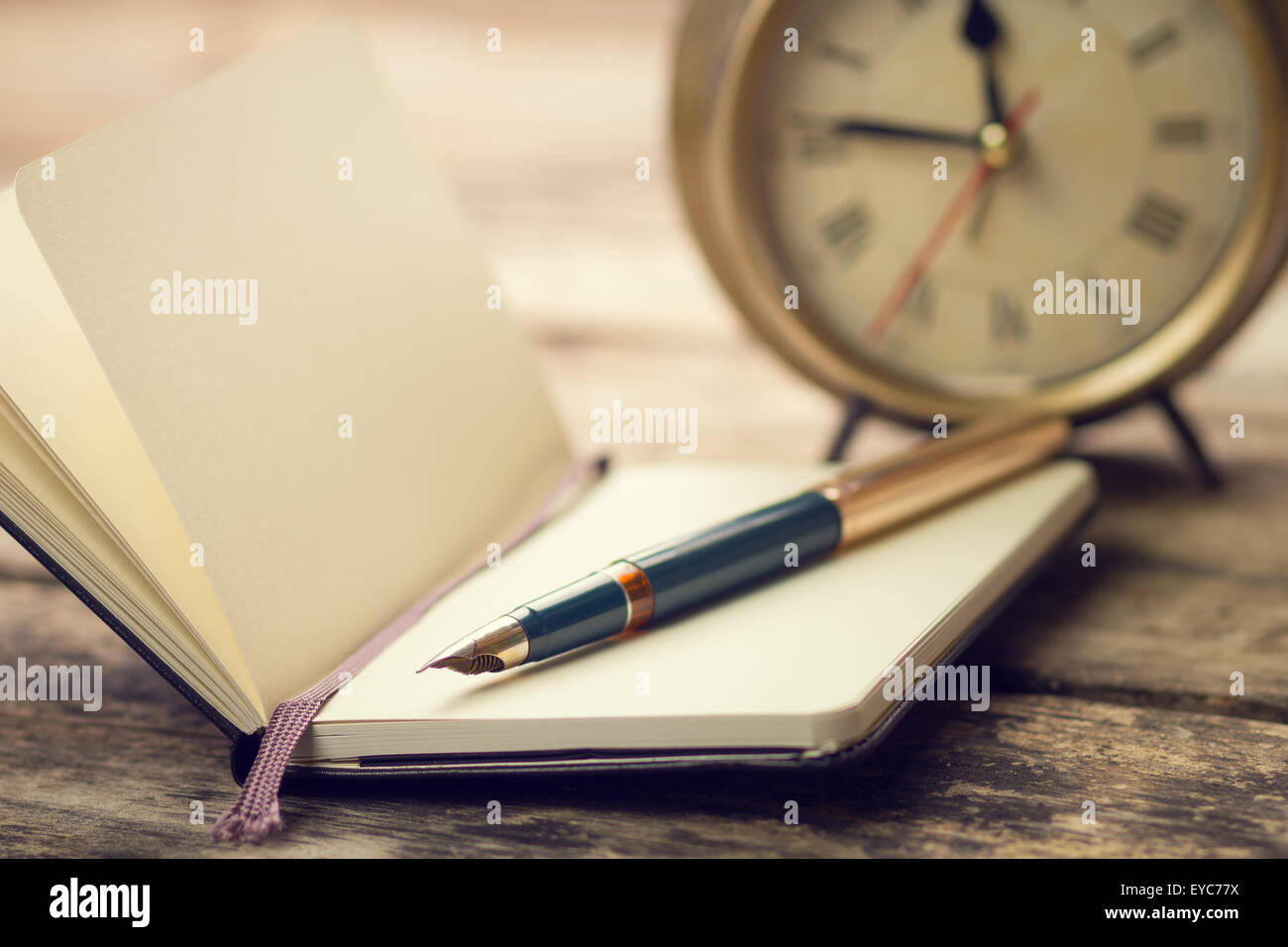 Offene kleine Notebook mit Füllfederhalter und altmodische Wecker hinter. Warme Farbe getönt Vintage Bild Stockfoto