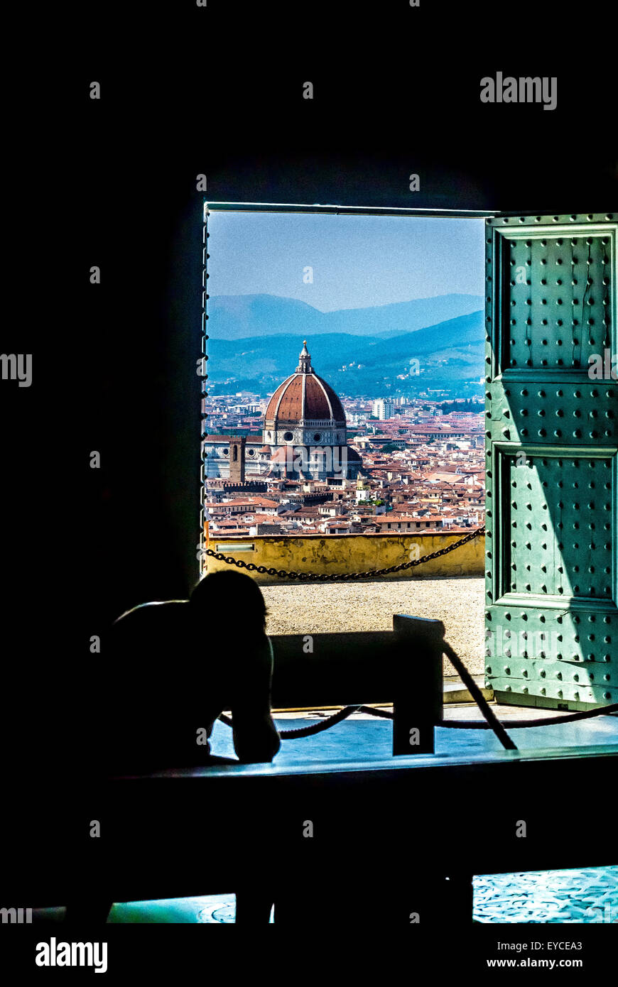 Silhouette eines Mannes, der in der Kirche San Miniato al Monte betet, mit der Kathedrale von Florenz, die durch die offene Tür gesehen wird. Florenz, Italien. Stockfoto