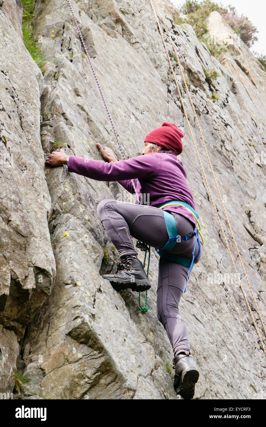 Weibliche Kletterer mit Seilsicherung Klettern auf einen Sprung in eine steile Felswand. North Wales, UK, Großbritannien Stockfoto