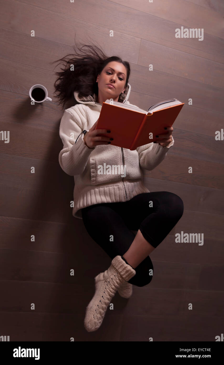 Schöne Frau liegend auf Holzboden und Buch mit Kaffee Stockfoto