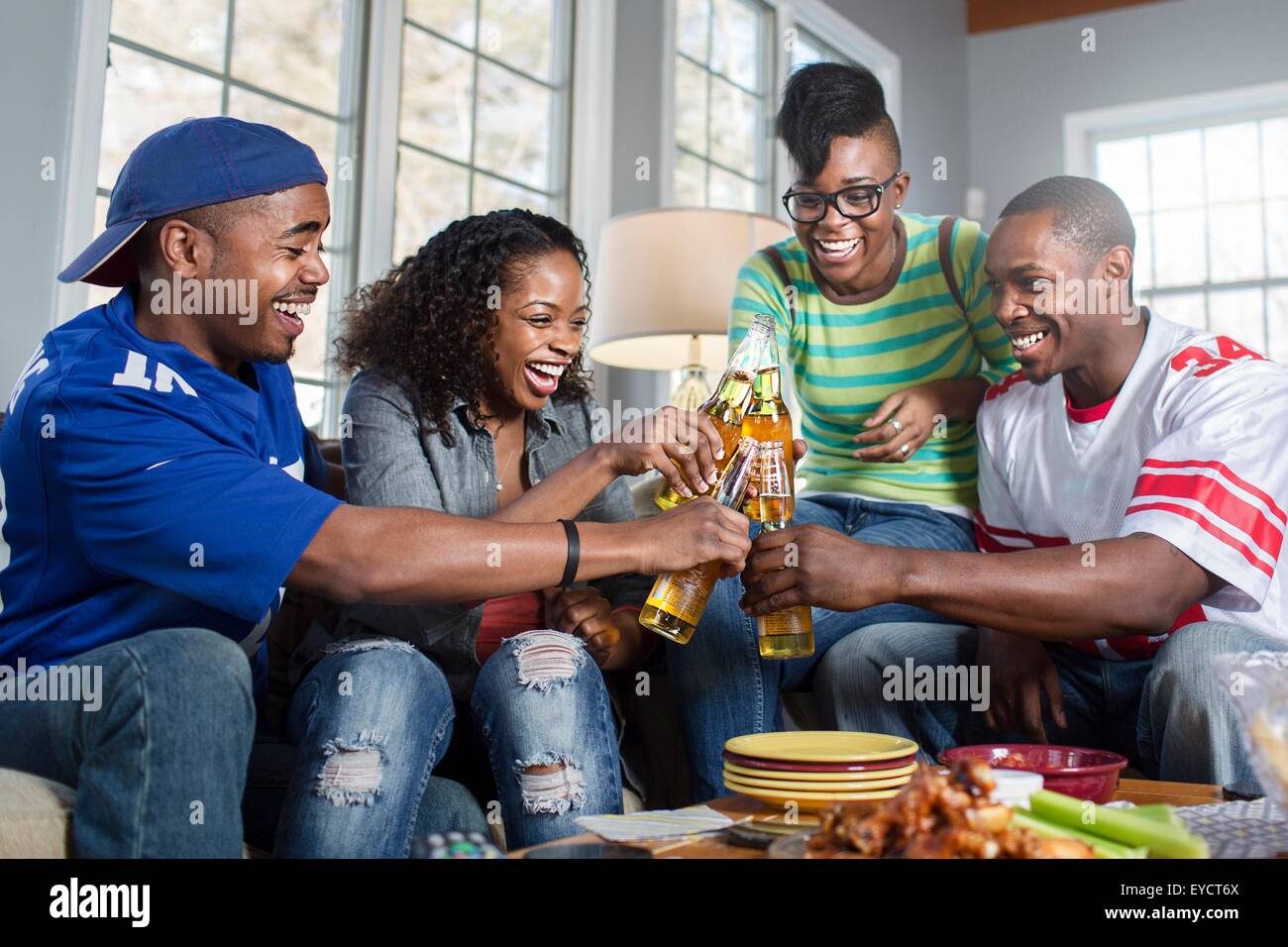 Vier Erwachsenen Freunden Toasten mit Flaschenbier auf Sofa im Wohnzimmer Stockfoto