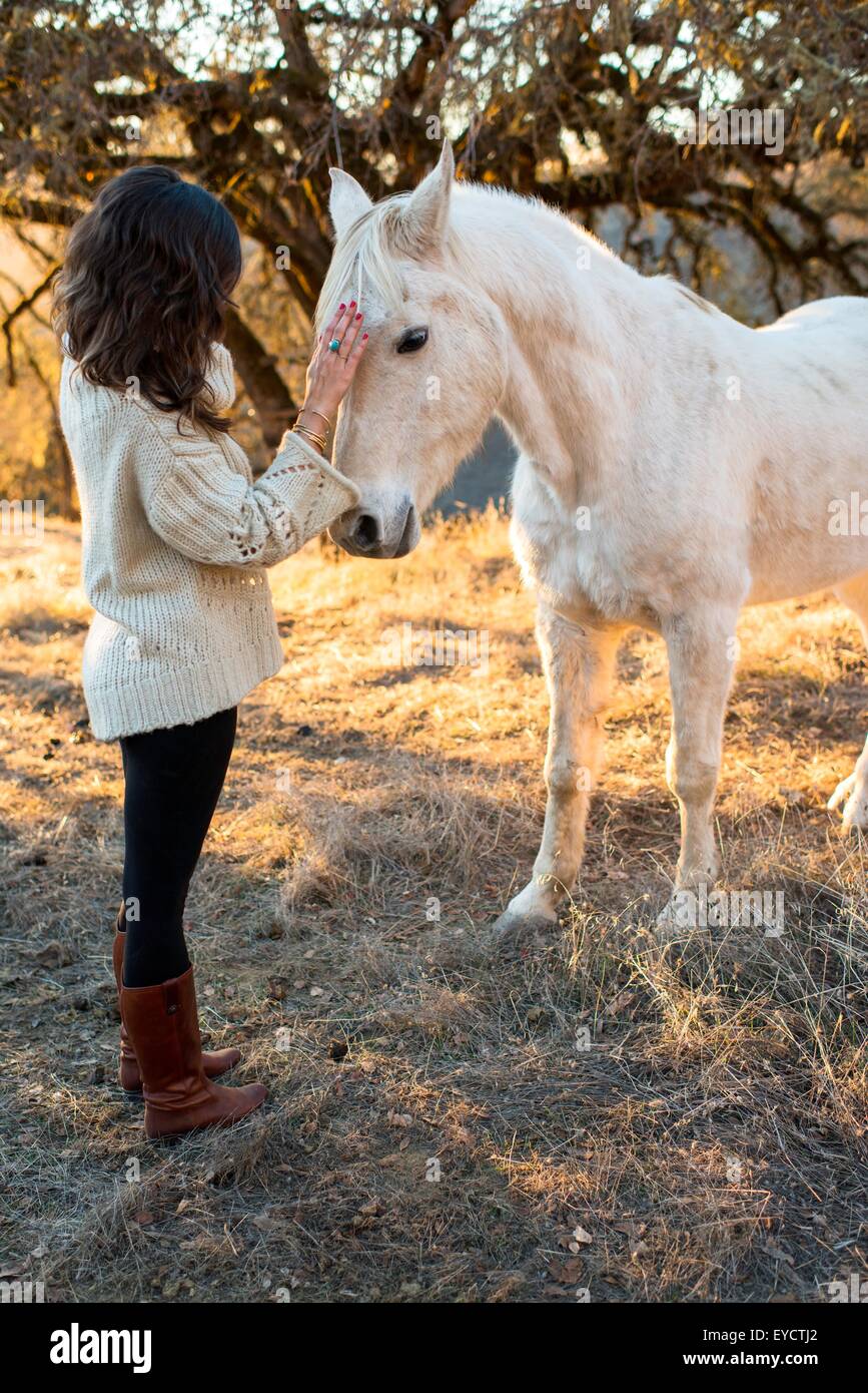 Junge Frau Petting weißes Pferd im Feld Stockfoto