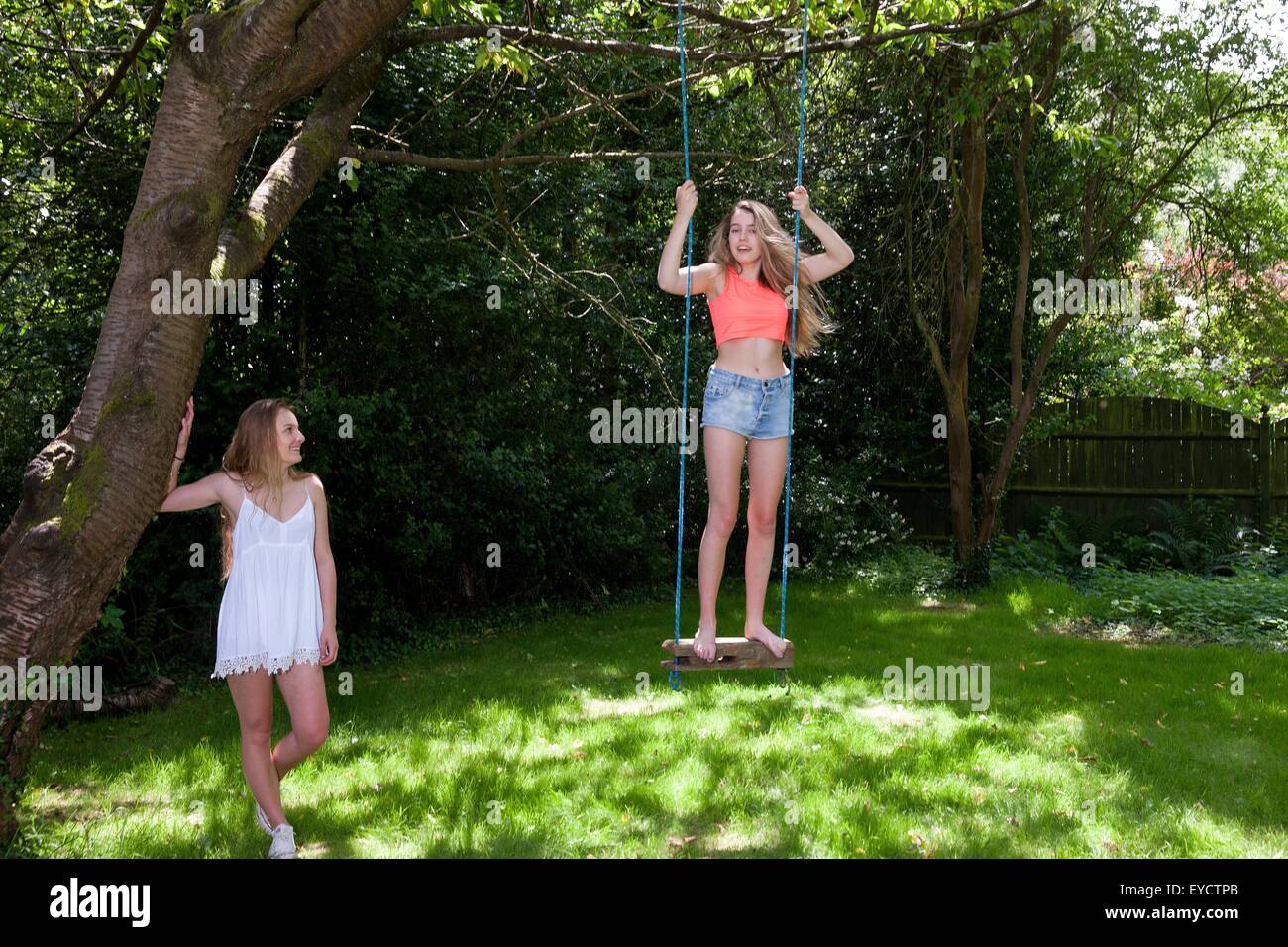 Teenager-Mädchen auf Baum schwingen, schwingen, während Freund auf Uhren Stockfoto