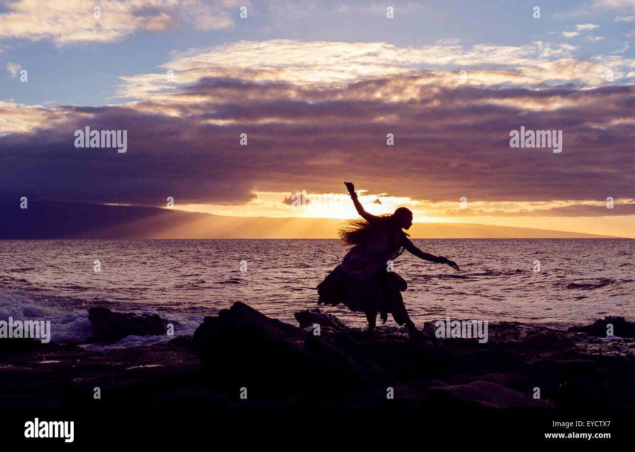 Silhouette Frau Hula tanzen auf Küstenfelsen tragen Tracht bei Sonnenuntergang, Maui, Hawaii, USA Stockfoto