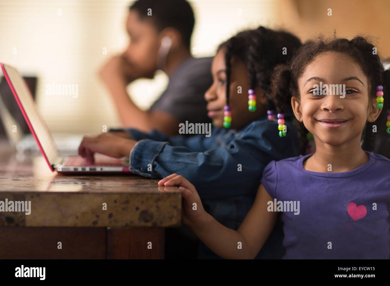 Porträt von Mädchen am Esstisch und Geschwister mit Notebooks Stockfoto