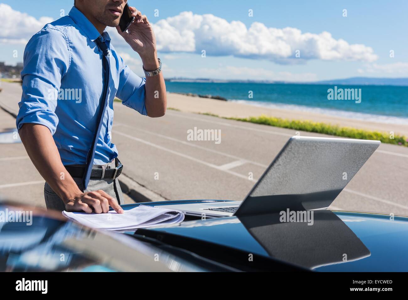 Junger Geschäftsmann auf Küste Parkplatz mit Laptop, während auf Smartphone sprechen Stockfoto