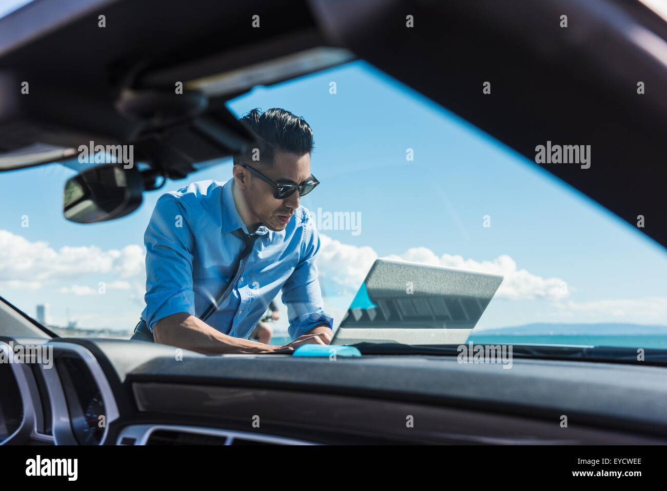 Junger Geschäftsmann auf Küste Parkplatz mit Laptop auf Motorhaube Stockfoto