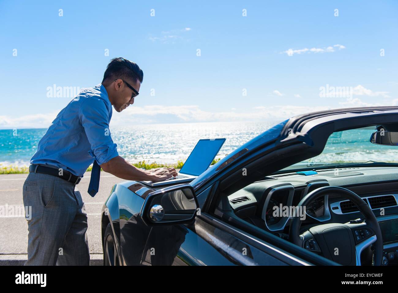 Junger Geschäftsmann auf Küste Parkplatz Tippen auf Laptop auf Motorhaube Stockfoto