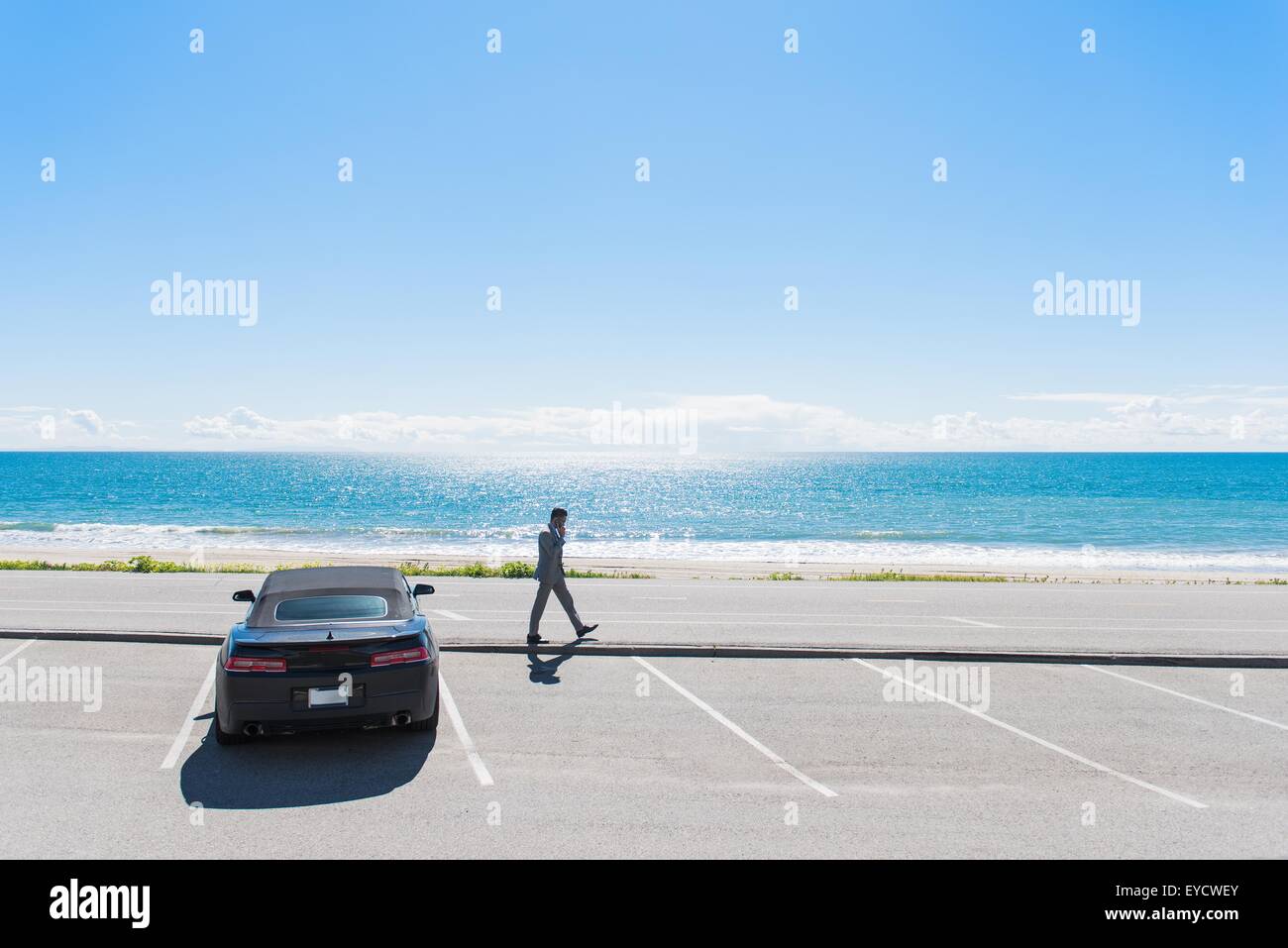 Junger Geschäftsmann an Küsten Parkplatz zu Fuß, während auf Smartphone sprechen Stockfoto