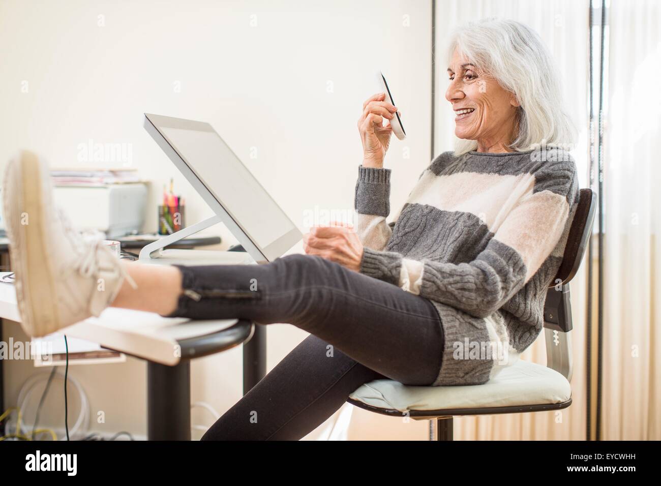 Porträt von senior Frau sitzt am Computer Schreibtisch Smartphone mit Fuß festhalten Stockfoto