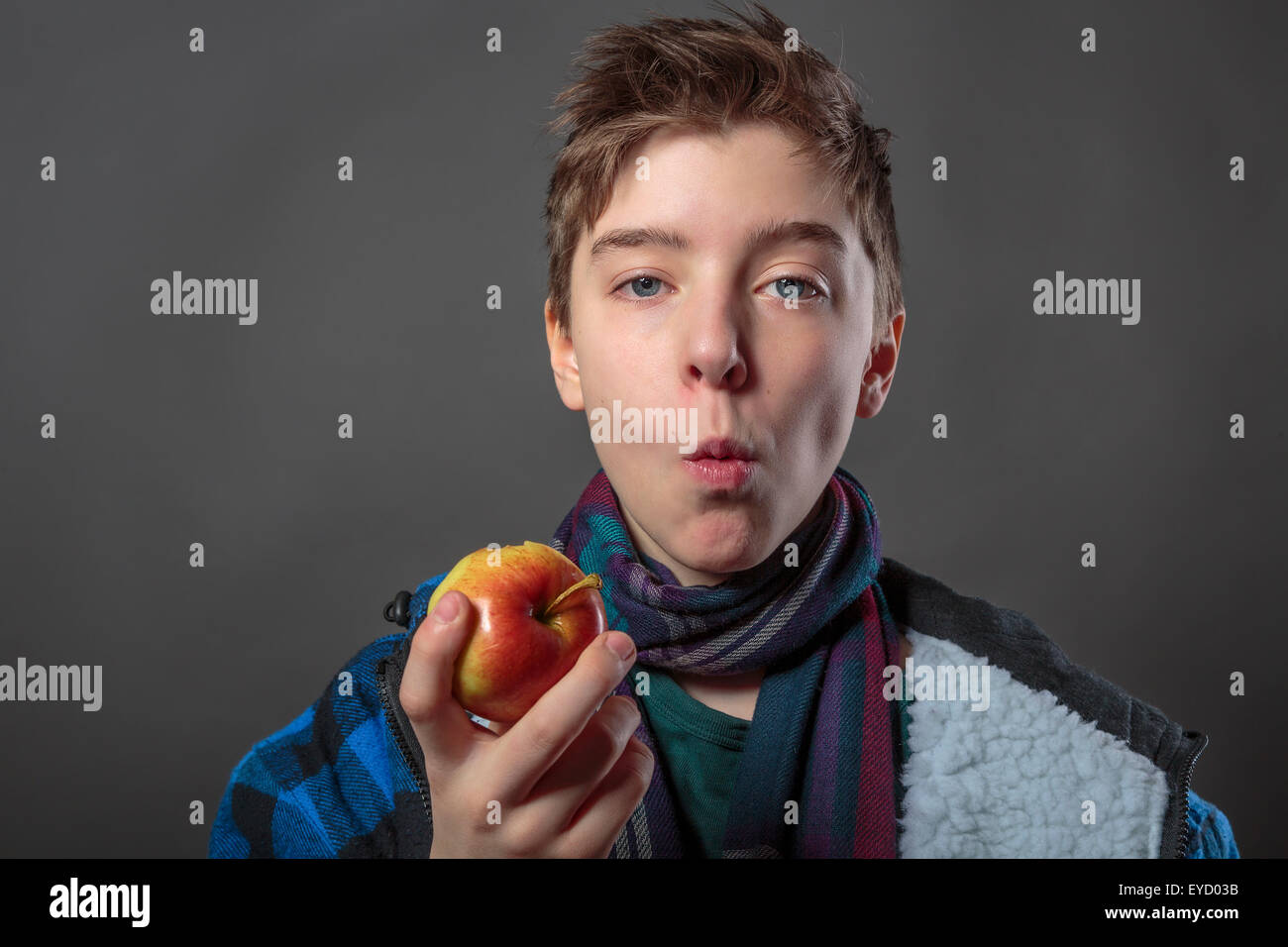 Porträt eines männlichen Jugendlichen Essen eines Apfels mit Winterjacke, isoliert auf grau Stockfoto