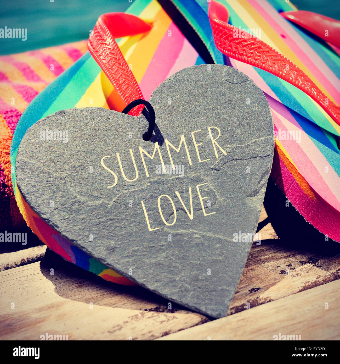 der Text Summer Love, geschrieben in einer herzförmigen Schiefer und ein paar Flip-Flops Regenbogen auf einem Holzsteg, leichte Vignette adde Stockfoto