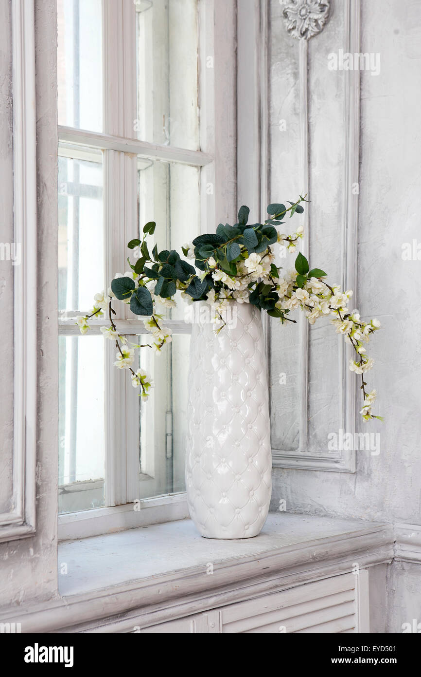 Stillleben mit Bouquet von künstlichen Kirschblüten in einer chinesischen Vase auf dem Fensterbrett in weiß innen Stockfoto