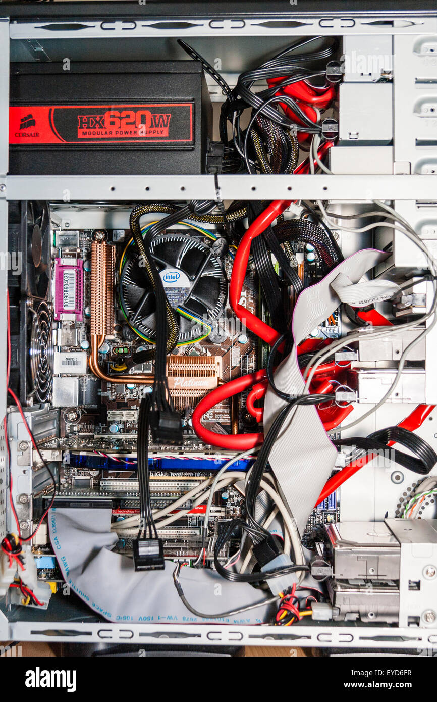 Innenraum des Computergehäuses mit der Hauptplatine und Prozesse Ventilator, plus Kupfer Kühlkörper, Kabel, Flachbandkabel und Festplatten. Überladen. Stockfoto