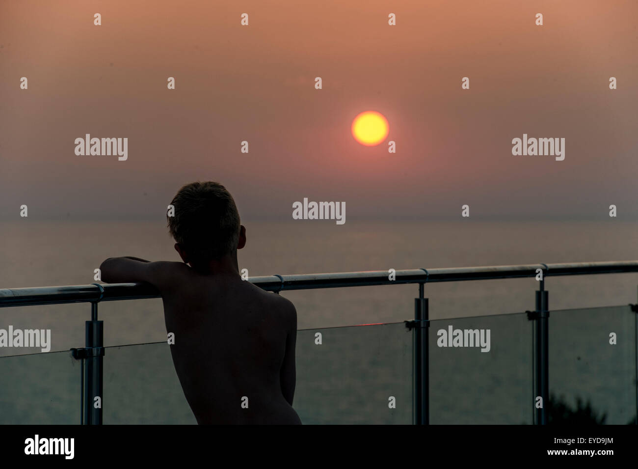 Ein Junge beobachtet den Sonnenuntergang von einer Glaswand im Urlaub Stockfoto