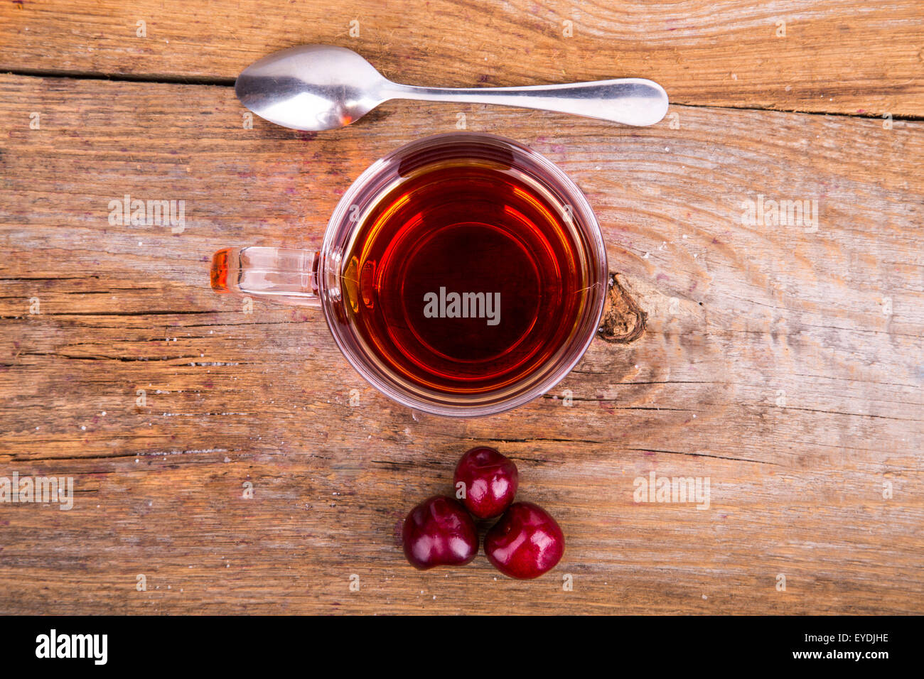 Tasse Tee, Löffel und süßen Kirschen auf einem hölzernen Hintergrund Stockfoto