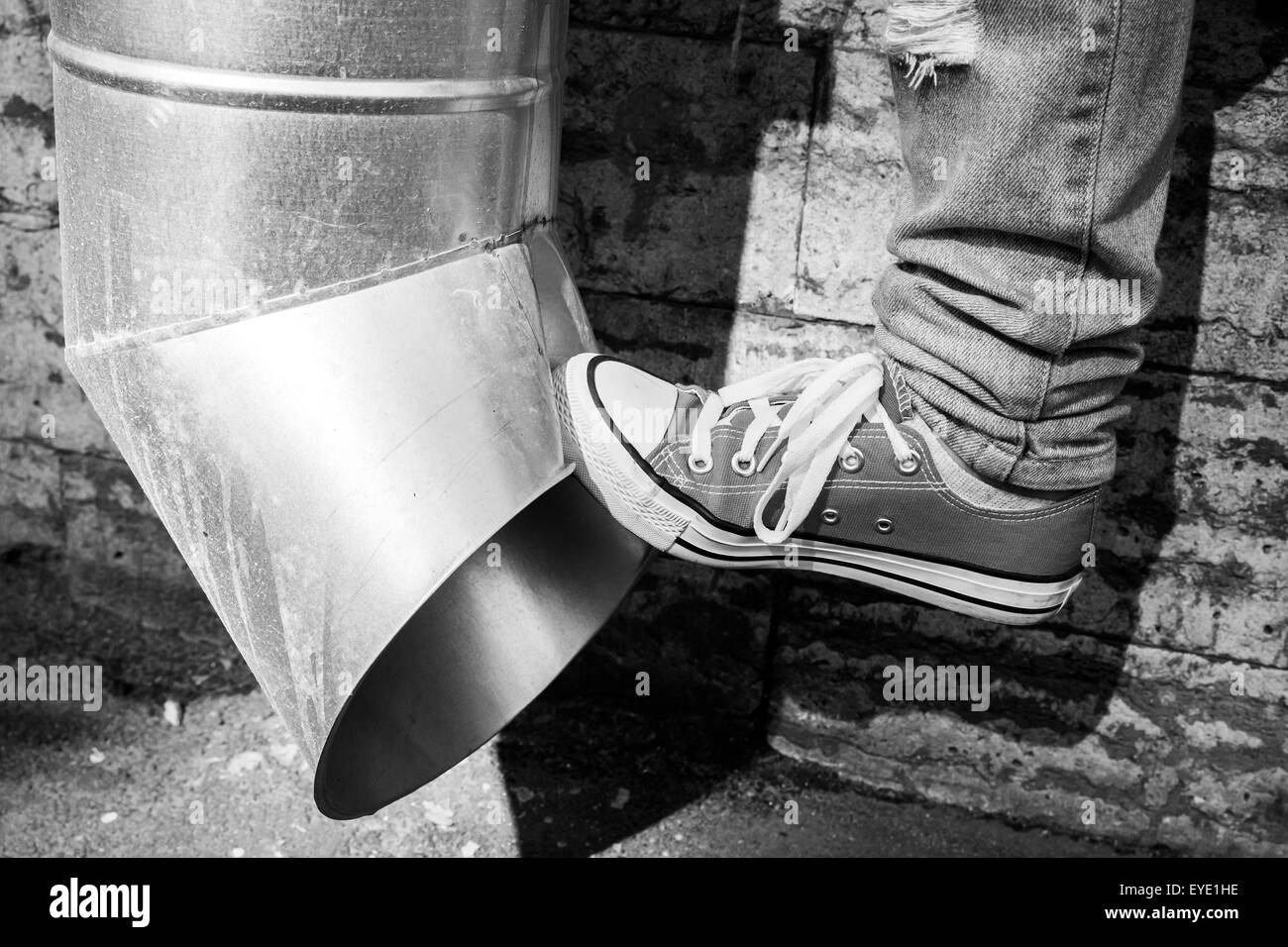 Teenager in Turnschuhen tritt urban Abflußrohr, schwarz / weiß Foto Stockfoto