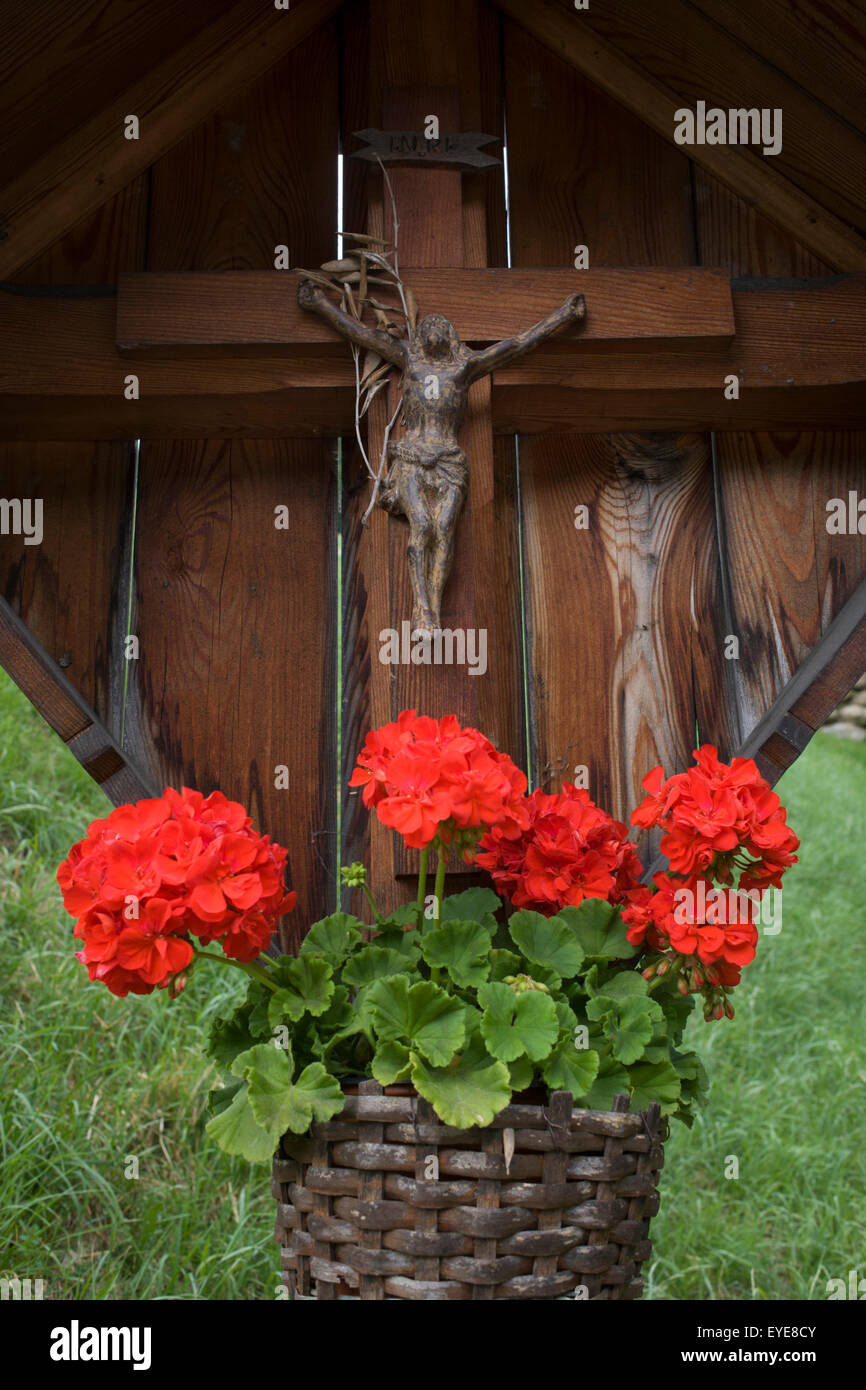 Ländlichen Kruzifix und rote Blumen auf einen am Straßenrand Schrein auf dem Jaufenpass in Südtirol, Norditalien. Stockfoto