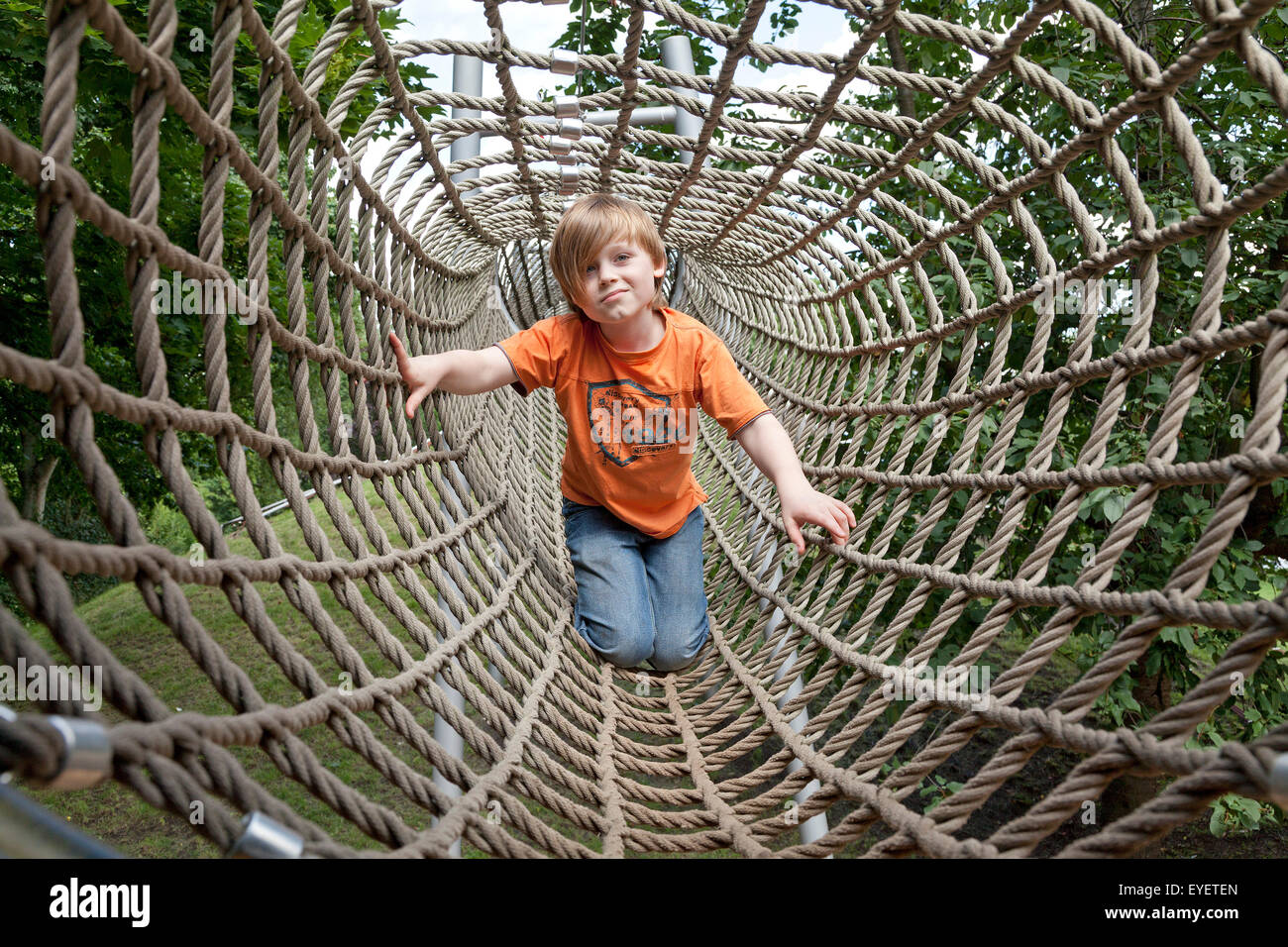 kleiner Junge Klettern durch ein Seil-Tunnel auf einem Spielplatz Stockfoto