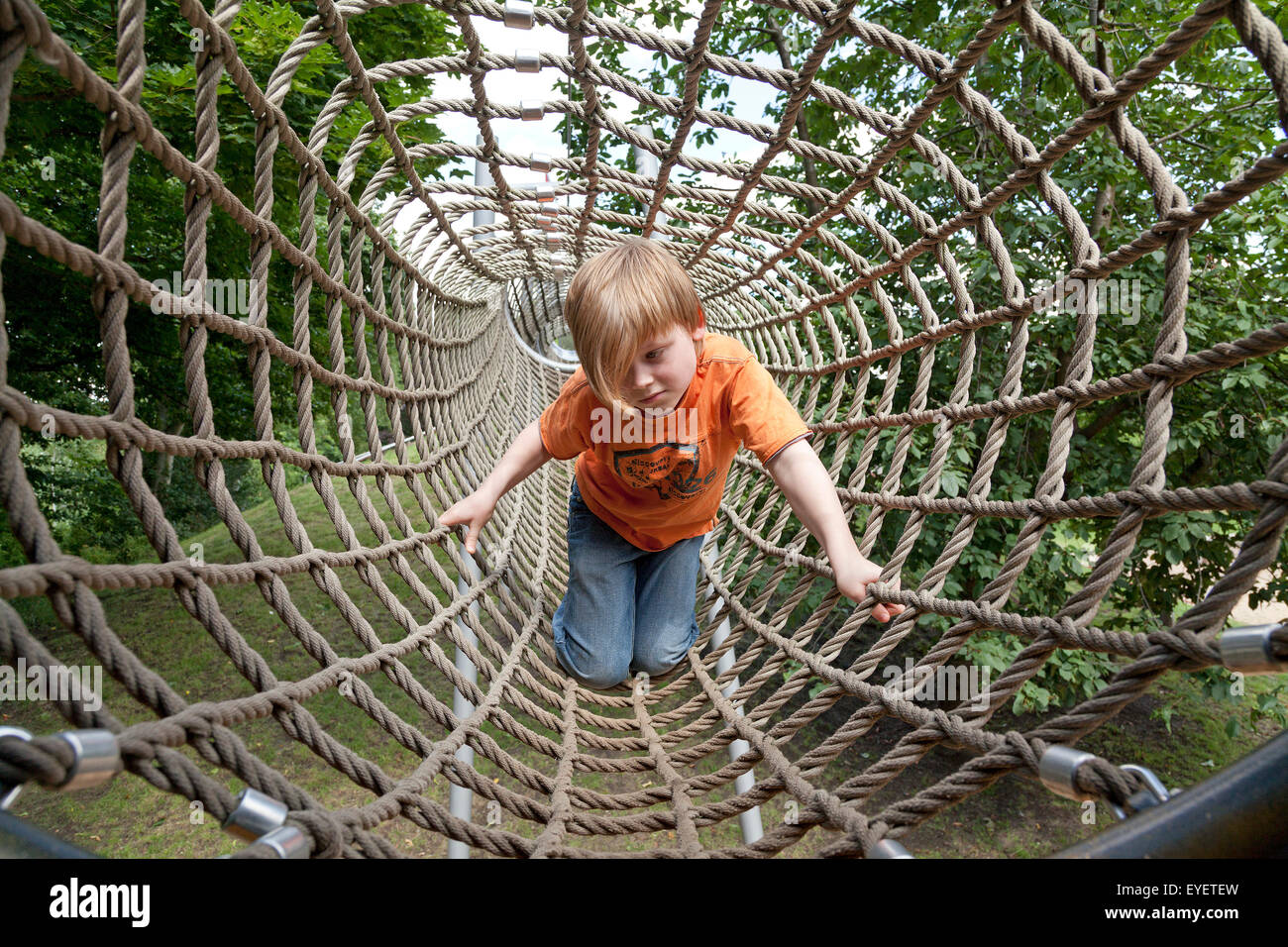 kleiner Junge Klettern durch ein Seil-Tunnel auf einem Spielplatz Stockfoto