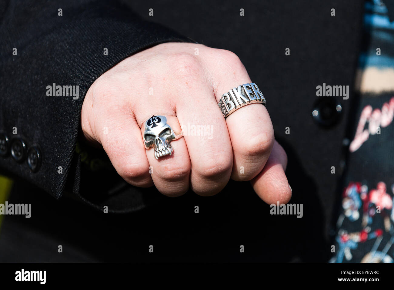 Ein Mann mit einer 'Biker' Ring an seine geballte Faust. Seine anderen Ring ist ein Schädel mit der Ace of Spades gekennzeichnet. Sowohl aus weißem Metall sind Stockfoto