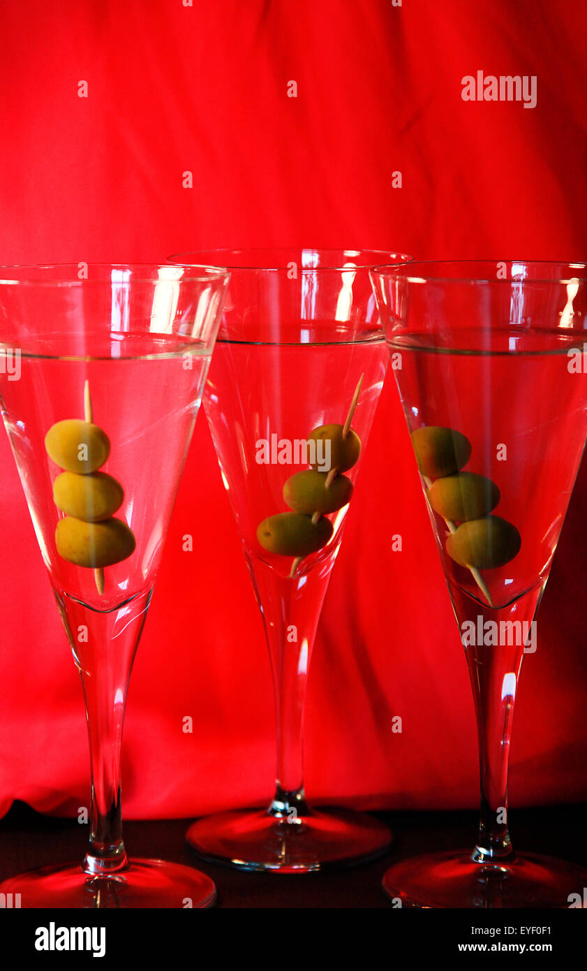 Drei Martini-Cocktails mit Oliven vor dem leuchtend roten Hintergrund Stockfoto