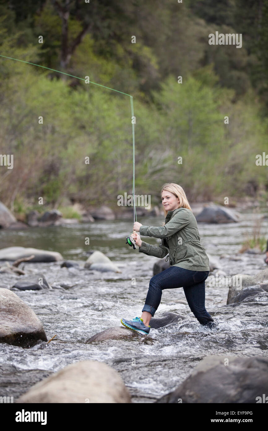 Eine junge, abenteuerlustige Frau in Jeans und eine grüne Jacke Fliegenfischen in einem schnell bewegten Fluss in die Berge der Sierra Nevada in Nordkalifornien. Stockfoto