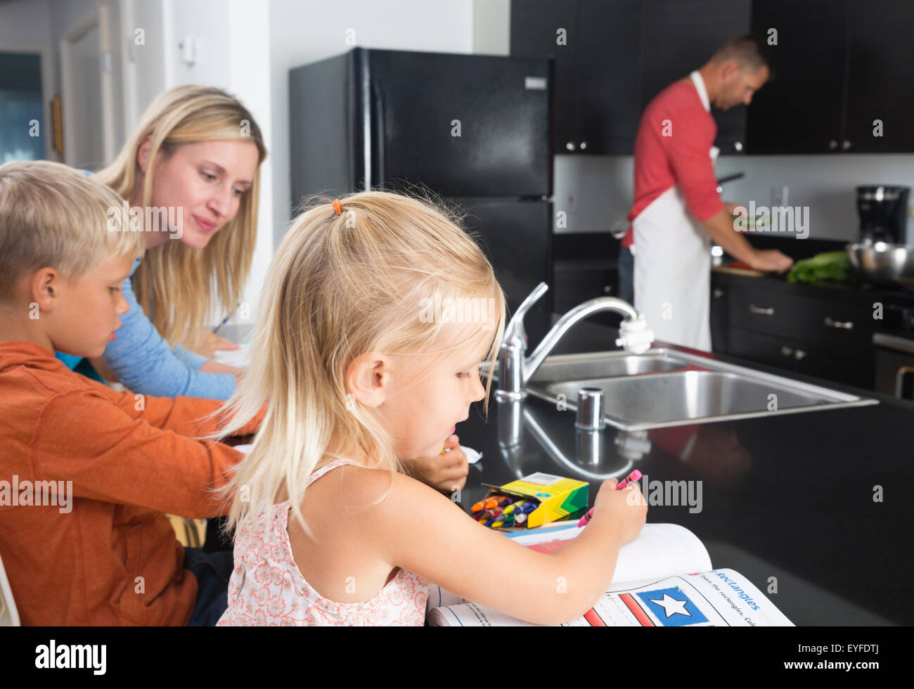 Mutter mit Sohn (10-11) und Tochter (2-3) und Vater Zubereitung Hausaufgaben Stockfoto